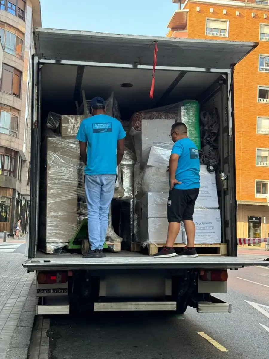 Dos mudadores de Ekuafran con camiseta azul de la empresa revisan la carga de un camión en la calle