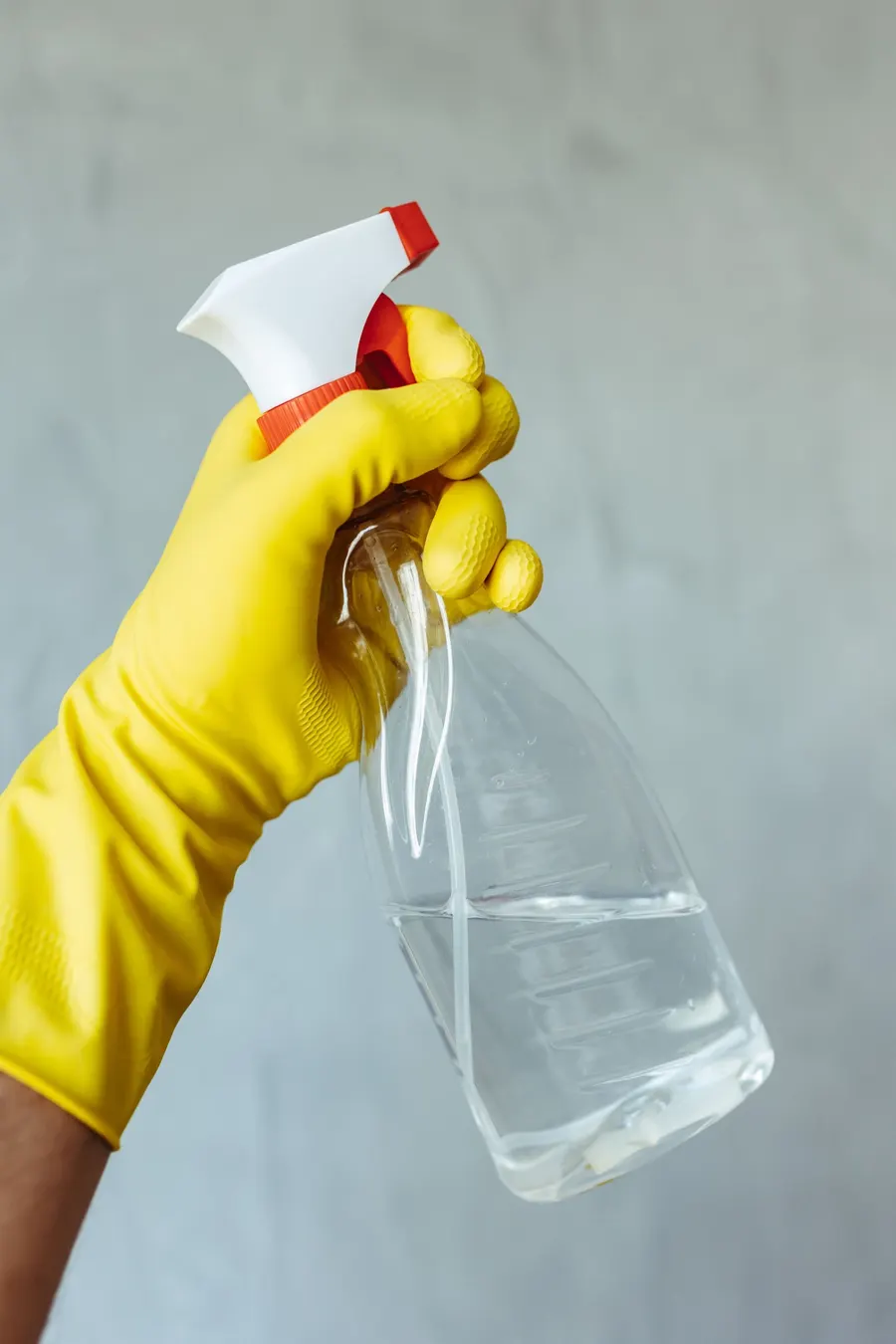 Mano con guante amarillo sujeta un pulverizador de limpieza